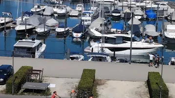 Weitläufiger Blick auf einen belebten Yachthafen mit zahlreichen Booten und dem weiten See unter strahlend blauem Himmel.