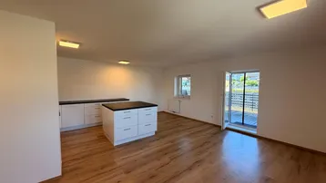 Helles, offenes Wohnzimmer mit Küchenzeile, Kücheninsel und Zugang zum Balkon.