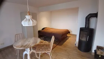 Gemütlicher Wohnbereich mit Holzboden, kleinem Esstisch und einem rustikalen Holzofen.