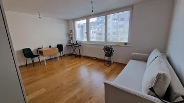 Helles Wohnzimmer mit Holzboden, beigem Sofa und großen Fenstern mit Blick auf die Umgebung.