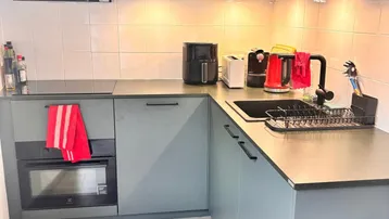 Moderne Küche mit grauen Schränken, integriertem Backofen und heller Arbeitsplatte.