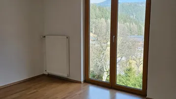 Helles Zimmer mit Laminatboden und großer Balkontür, die einen weiten Blick auf die Berge ermöglicht.