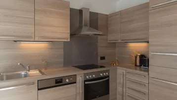 Moderne Einbauküche mit holzfarbenen Fronten, integrierten Geräten und Dunstabzugshaube.