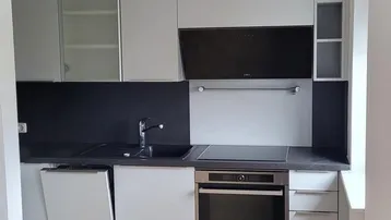 Moderne Einbauküche mit hellgrauen Fronten, dunkler Arbeitsplatte und Parkettboden.