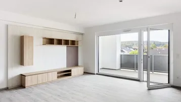 Geräumiges Wohnzimmer mit Holzelementen, Laminatboden und großem Balkonzugang, der viel Tageslicht hereinlässt.