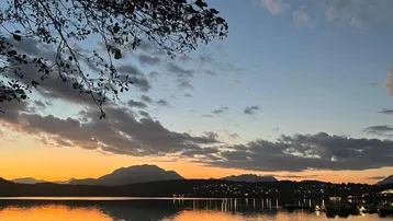 Malerischer Sonnenuntergang über einem See mit Bergen im Hintergrund und ruhigem Wasser.