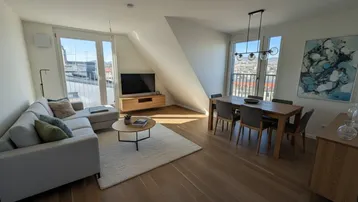 Helles Wohn- und Esszimmer mit Holzboden, modernen Möbeln und Zugang zu einem Balkon.