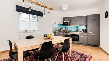 Moderne Küche mit Esstisch, grauen Schränken und Holzboden, ideal für gemeinsame Mahlzeiten.