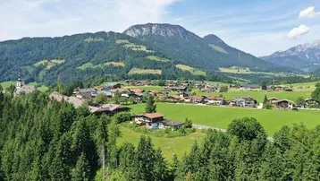 Panoramablick auf ein idyllisches Bergdorf, umgeben von grünen Wäldern und majestätischen Bergen.