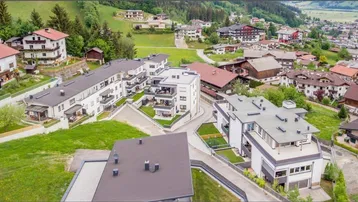 Luftaufnahme einer modernen Wohnsiedlung mit mehreren Gebäuden in grüner Umgebung.
