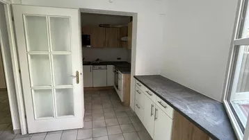 Heller Küchenbereich mit Fliesenboden, Arbeitsplatte am Fenster und Blick in die separate Küche.