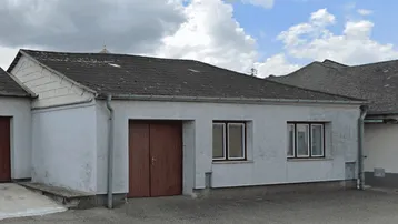 Gebäudeaußenansicht mit Garagentor und schlichten Fenstern unter bewölktem Himmel.