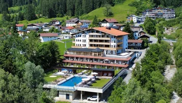 Luftaufnahme eines luxuriösen Hotelkomplexes mit Außenpool und Bergblick in grüner Umgebung.