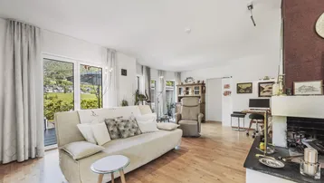 Helles Wohnzimmer mit gemütlichem Sofa, Kamin und großen Fenstern mit Bergblick.