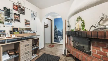 Eingangsbereich mit rustikalem Ziegelkamin, Holzboden und Informationsmaterial.