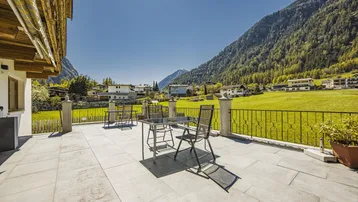 Geräumige Terrasse mit Bergblick und Sitzgelegenheiten, umgeben von grünen Wiesen.