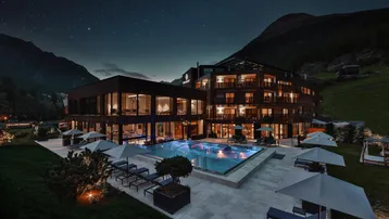 Luxuriöses Hotelgebäude mit beleuchtetem Außenpool und Liegebereichen unter sternenklarem Nachthimmel.