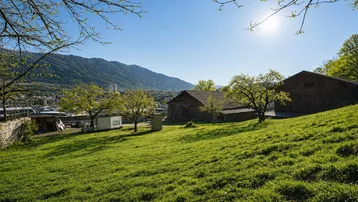 Sonnige grüne Wiese mit Blick auf die Stadt und die umliegenden Berge.