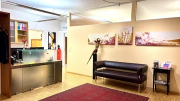 Empfangsbereich mit Wartebereich, dunklem Sofa, rotem Teppich und Holzfußboden in einem Büro.