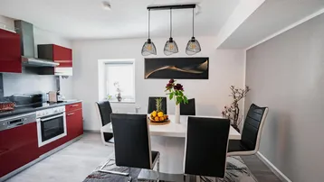 Moderne offene Küche mit Essbereich, roten Hochglanzfronten und stilvollen Pendelleuchten.