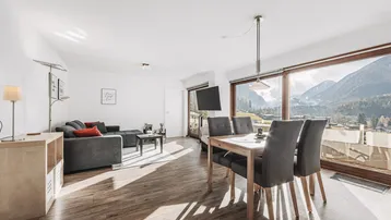 Helles Wohn- und Esszimmer mit Holzboden, gemütlicher Sitzecke und beeindruckendem Bergblick.
