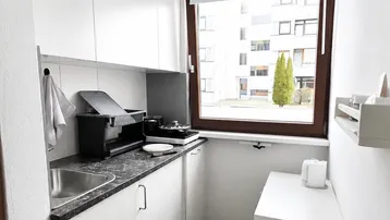 Kleine, helle Küche mit weißen Schränken, dunkler Arbeitsplatte und Fensterblick.