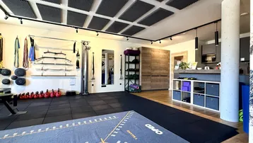 Großer, offener Raum, eingerichtet als Fitnessstudio mit Trainingsgeräten und schallabsorbierenden Deckenplatten.