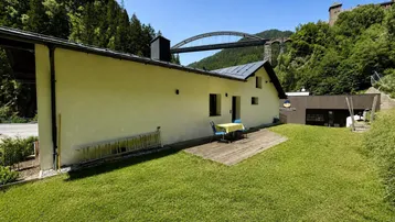 Gepflegter Rasenbereich mit kleiner Holzterrasse und Fernblick auf eine Brücke.