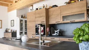 Moderne Holzküche mit dunkler Arbeitsplatte, integrierten Geräten und sichtbaren Deckenbalken.
