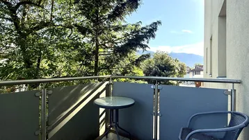 Balkon mit Metallgeländer, Fliesenboden und weitem Blick auf die umliegenden Berge und Bäume.