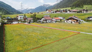 Luftaufnahme eines grünen Feldes mit gelben Blumen, umgeben von Häusern und Bergen.