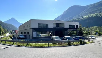 Modernes Geschäftsgebäude mit großen Fenstern und Parkplätzen, umgeben von einer beeindruckenden Berglandschaft.