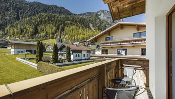 Holzbalkon mit Blick auf ein Dorf, eine Kirche und die umliegende Berglandschaft.
