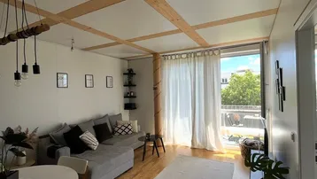 Heller Wohn- und Essbereich mit Holzbalkendecke, Parkettboden und Zugang zum Balkon.