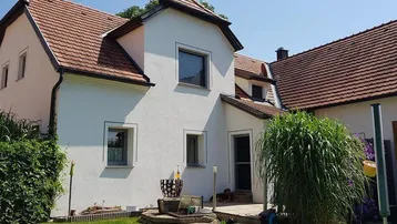 Seitenansicht eines Einfamilienhauses mit kleiner Holzterrasse und gepflegtem Gartenbereich.