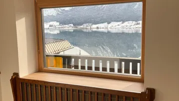 Heller Raum mit Holzboden, Fensterbank und beeindruckendem Seeblick auf verschneite Berge.