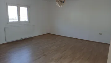 Helles, leeres Zimmer mit Laminatboden und großem Fenster, bereit zur individuellen Gestaltung.