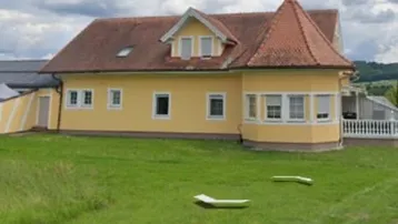 Gelbes Einfamilienhaus mit rotem Ziegeldach, kleinem Turm und großem Rasenbereich.