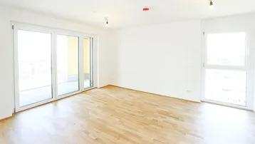 Helles, leeres Zimmer mit Parkettboden und großzügigem Zugang zu einem Balkon.
