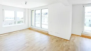 Helles Zimmer mit Parkettboden, großen Fenstern und Zugang zu einem Balkon.