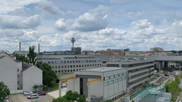 Weitläufiger Blick über die Stadt mit modernen Gebäuden und einem Fernsehturm unter bewölktem Himmel.