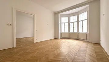 Helles Wohnzimmer mit Fischgrätparkett und einem charakteristischen Erkerfenster, das viel Tageslicht hereinlässt.