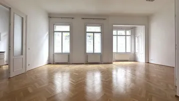 Helles, leeres Zimmer mit Fischgrätparkett und großen Fenstern, die viel Tageslicht hereinlassen.