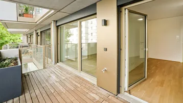 Geräumiger Balkon mit Holzboden, Pflanzkübeln und Zugang zu einem hellen Innenraum.