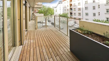 Geräumiger Balkon mit Holzfußboden, Glasgeländer und Blick auf die umliegende Stadtstraße.