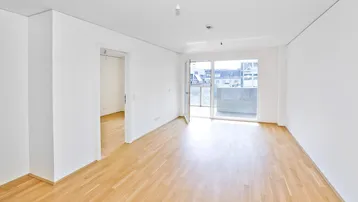 Helles, leeres Zimmer mit Parkettboden und Zugang zu einem Balkon, ideal für Wohn- oder Schlafbereich.
