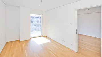 Helles Zimmer mit Holzboden und Zugang zu einem Balkon, ideal als Wohn- oder Schlafbereich.