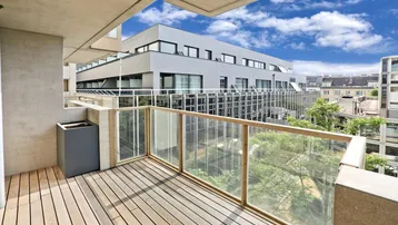 Moderner Balkon mit Holzfußboden und Glasgeländer, bietet einen Blick auf umliegende Gebäude.