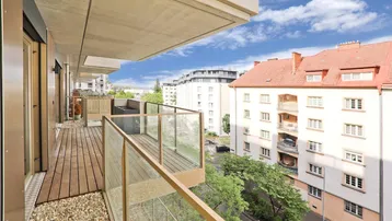 Moderner Balkon mit Holzfußboden, Glasgeländer und Blick auf die umliegenden Gebäude und die Straße.
