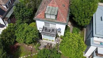 Luftaufnahme eines Hauses mit Garten, Balkon und umliegender grüner Landschaft unter blauem Himmel.